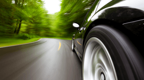 A close-up photo of a car driving down a road surrounded by trees.