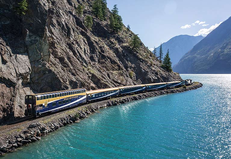 a train traveling on the tracks in between a mountainside and a river